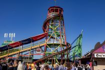 Toboggan (Konrad) - Wiesn-Attratkion - Laufgeschäft - Bilder - Auffällig ist der hohe Turm, an dem sich die Rutsche entlang schlängelt. Hinauf geht es teilweise mit einem Förderband, was leichter klingt als es ist und für so manchen Lacher der Zuschauenden sorgt. • © kirmesecke.de